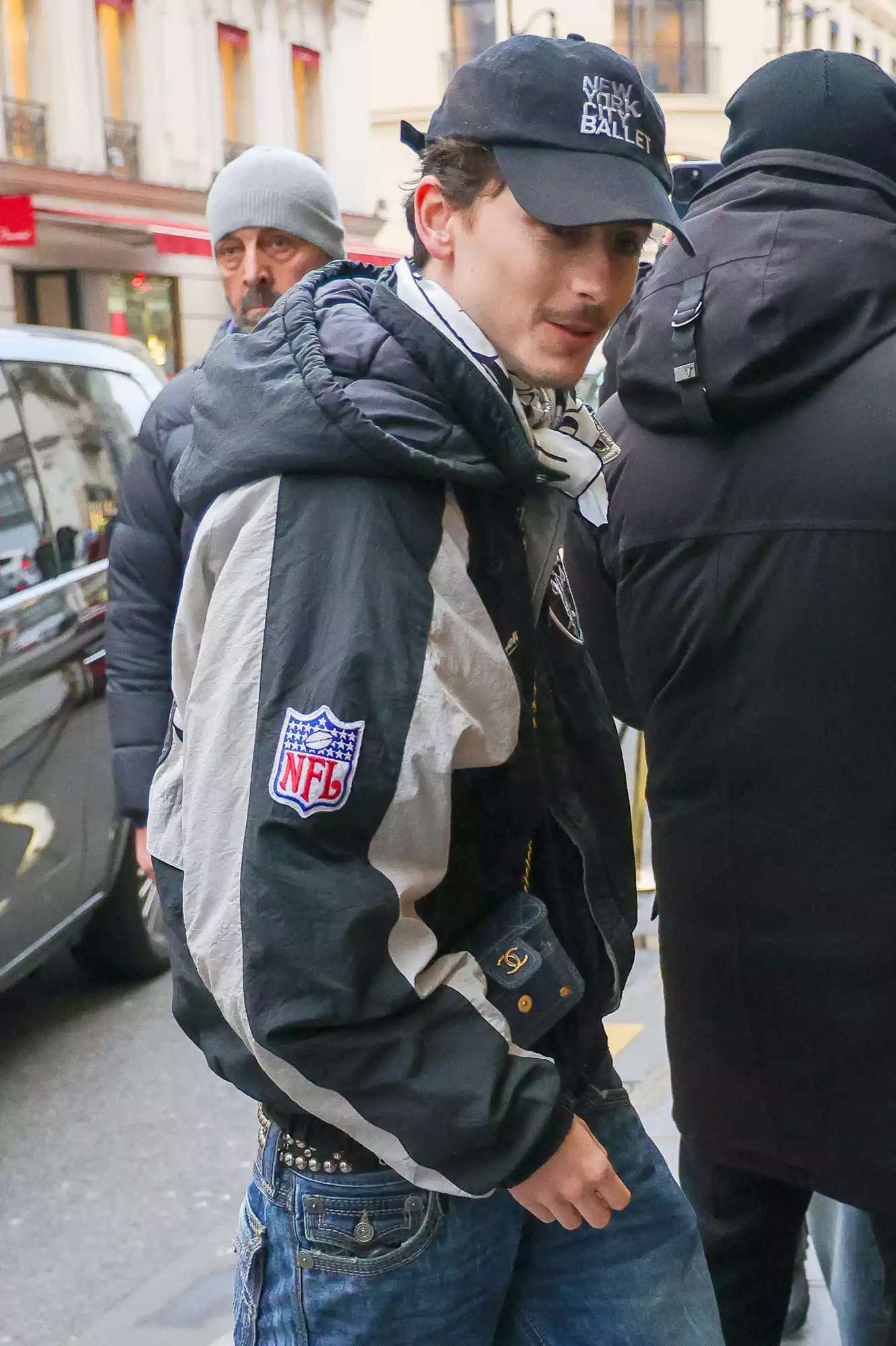 Actor Timothee Chalamet cuts a stylish figure in a Raiders Jacket paired with jeans, a mini Chanel bag, and a New York City Ballet Cap as he signs autographs for his fans while returning to his hotel in Paris.