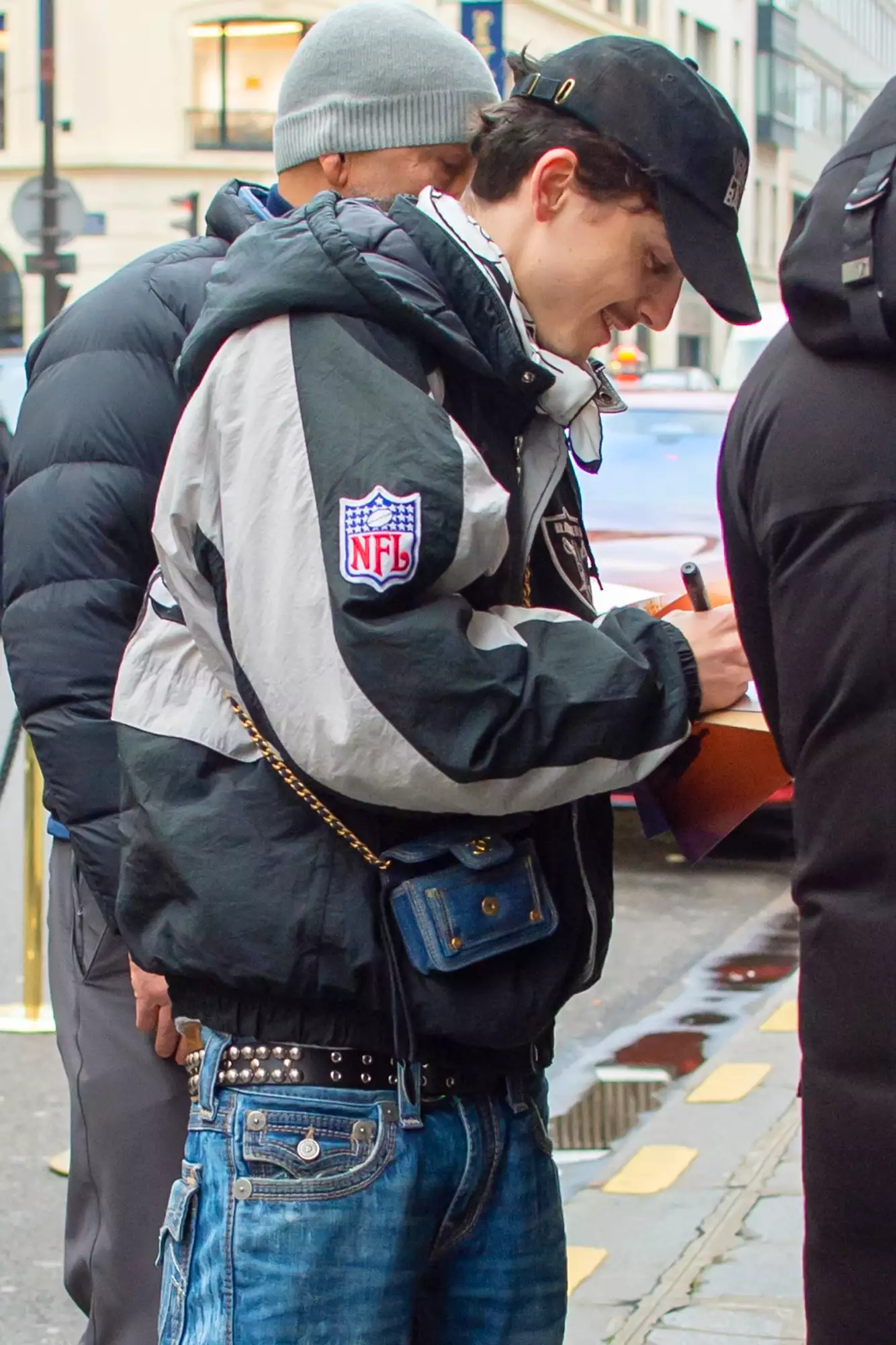 Actor Timothee Chalamet cuts a stylish figure in a Raiders Jacket paired with jeans, a mini Chanel bag, and a New York City Ballet Cap as he signs autographs for his fans while returning to his hotel in Paris.