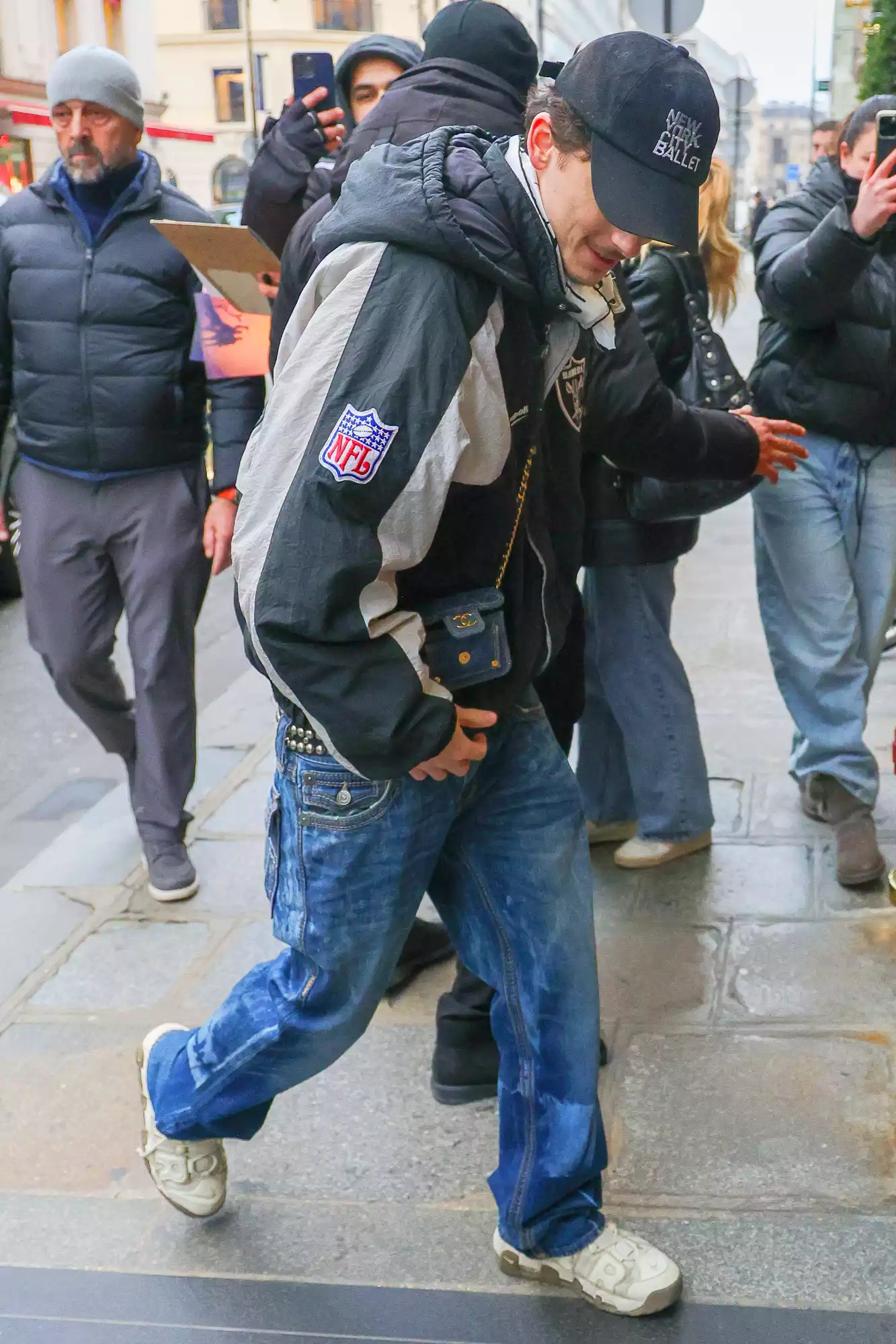 Actor Timothee Chalamet cuts a stylish figure in a Raiders Jacket paired with jeans, a mini Chanel bag, and a New York City Ballet Cap as he signs autographs for his fans while returning to his hotel in Paris.